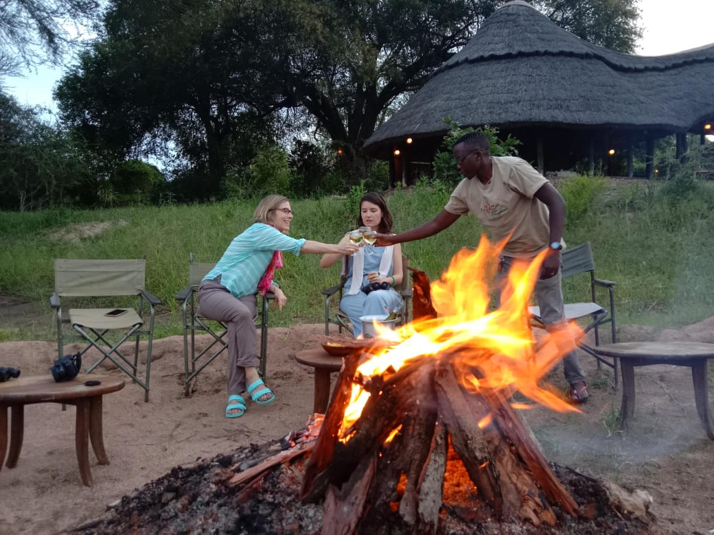 Guests sharing a sundowner toast around a vibrant bush campfire with their Olympus Adventure driver-guide